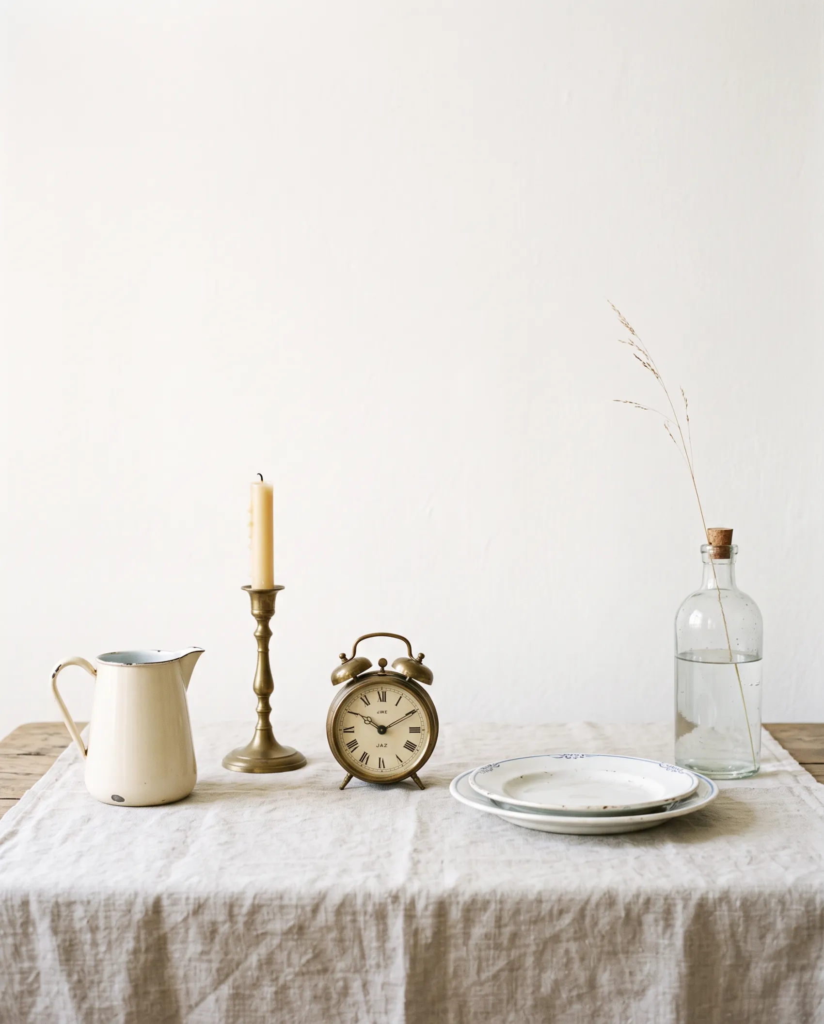 Table de brocante couverte d’objets anciens : pichets émaillés, bougeoirs, réveil, vaisselle